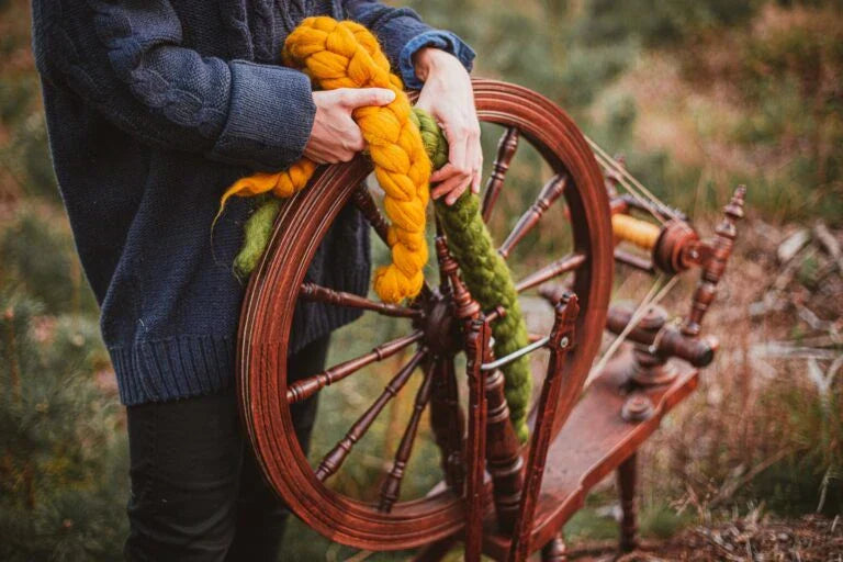 : Person mit Spinnrad im Freien hält Kammzüge aus bunter Wolle – ideal für den Einstieg ins Spinnen mit dem Spinnrad.