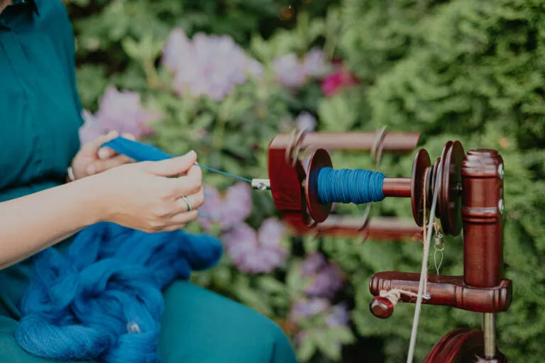 Spinnen mit dem mahagonifarbenen Kromski Sonata Encore Spinnrad im Garten mit blühenden Sträuchern